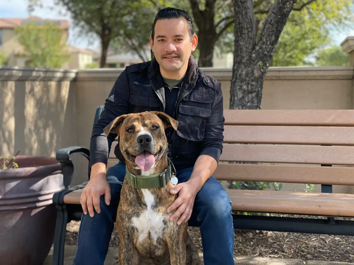 Robert Velazquez of AZ Dog Boss sitting on a park bench with a brindle dog